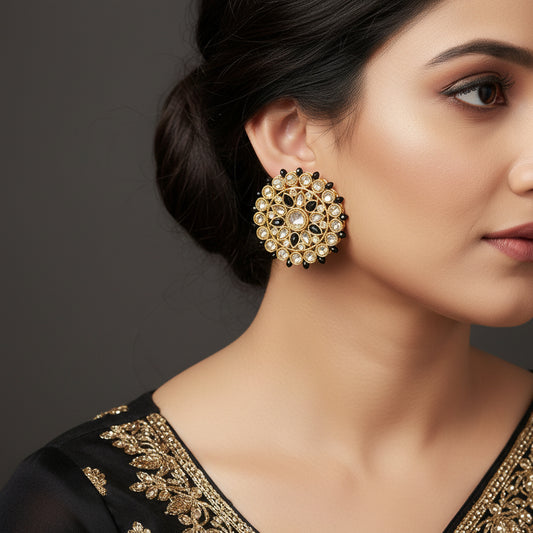 Gold and black earrings with gemstones on a dark background, featuring the brand 'Saheli'.