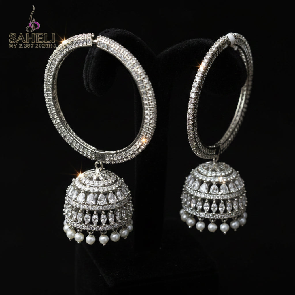 Silver hoop earrings with spherical embellishments on a dark stand against a gray background.
