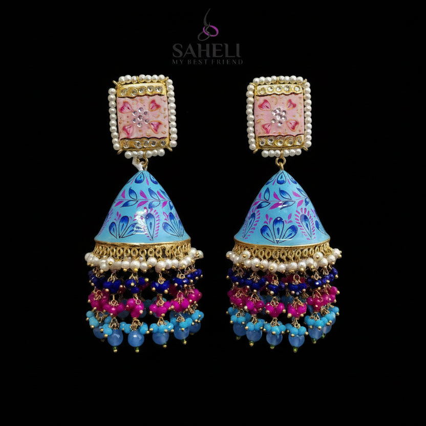 Colorful earrings with intricate designs on a gray background, featuring the brand 'Saheli'.