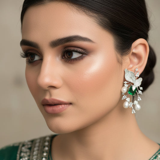 Pair of silver earrings with green and clear gemstones on a gray cushion