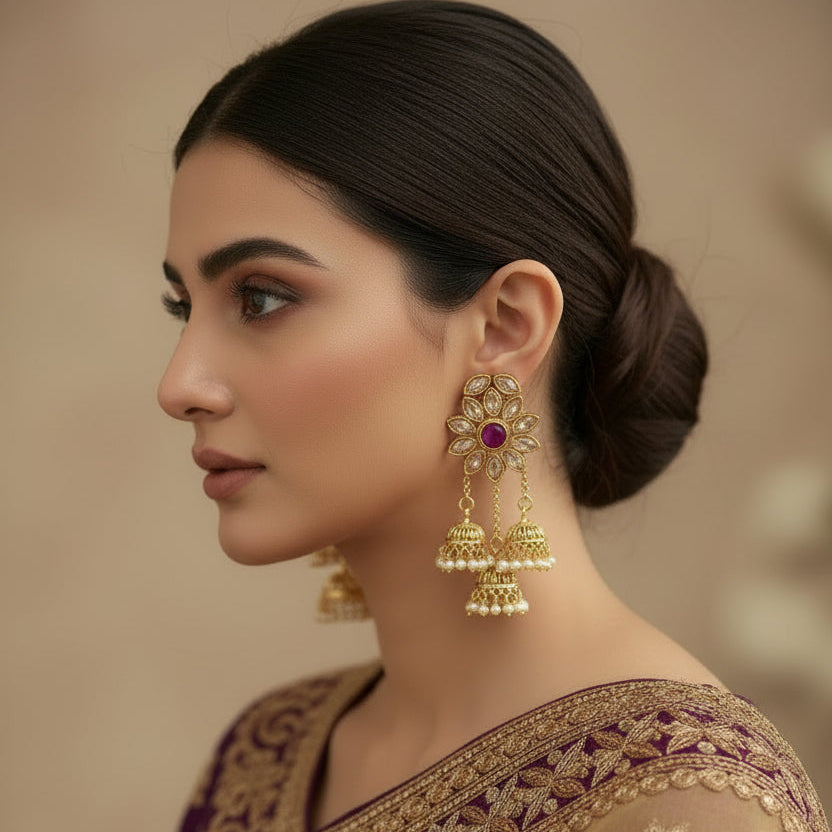 Gold earrings with pink gemstones on a black stand against a gray background, branded 'SAHELI'.