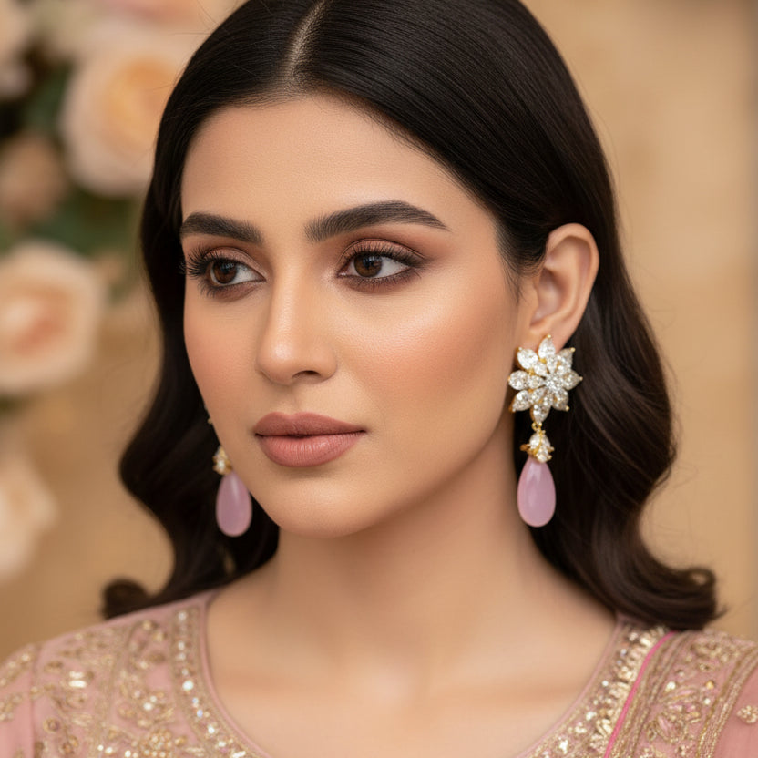 Pair of earrings with floral designs and pink teardrop stones on a dark background