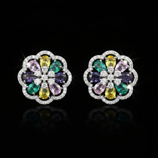A pair of round floral stud earrings in silver-tone metal, featuring a multicolor gemstone center with yellow, green, purple, and pink stones surrounded by clear crystals, set against a solid blue background.