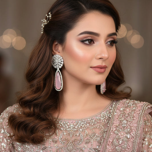 Pair of earrings with diamond-like stones and pink teardrop shapes on a gray cushion.