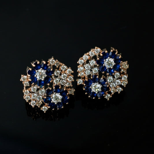 Pair of earrings with blue and silver design on a dark background, featuring the brand 'Saheli'.