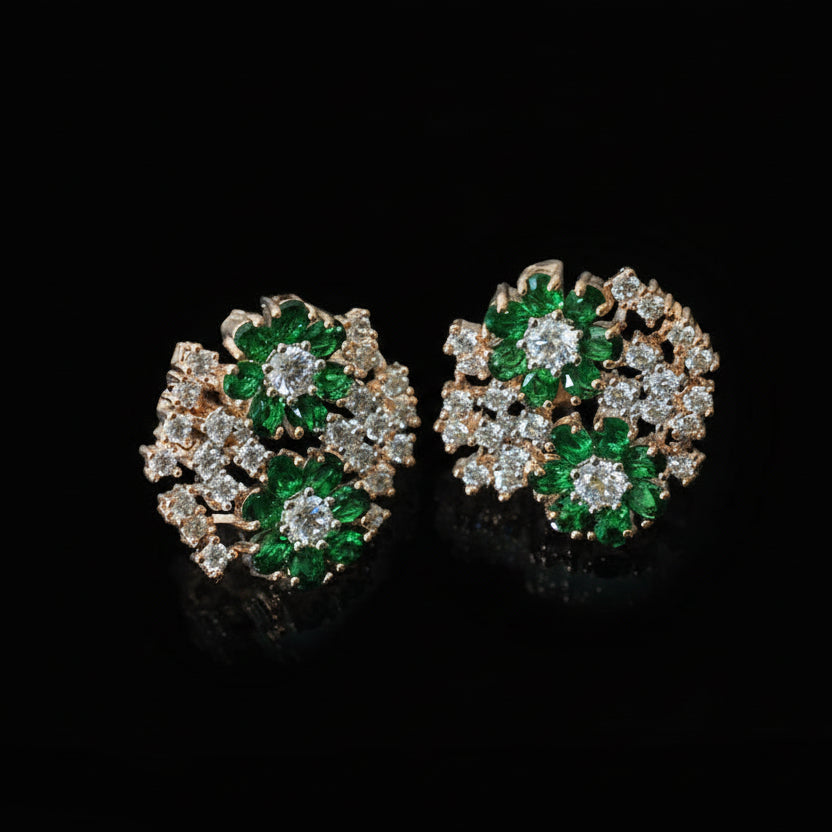 Pair of earrings with green gemstones and clear stones on a dark background, branded 'Saheli'.