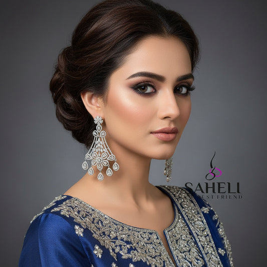 Pair of silver chandelier earrings with clear stones on a dark background, branded 'Saheli'.