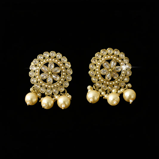 Pair of gold earrings with floral designs and pearl-like beads on a dark background
