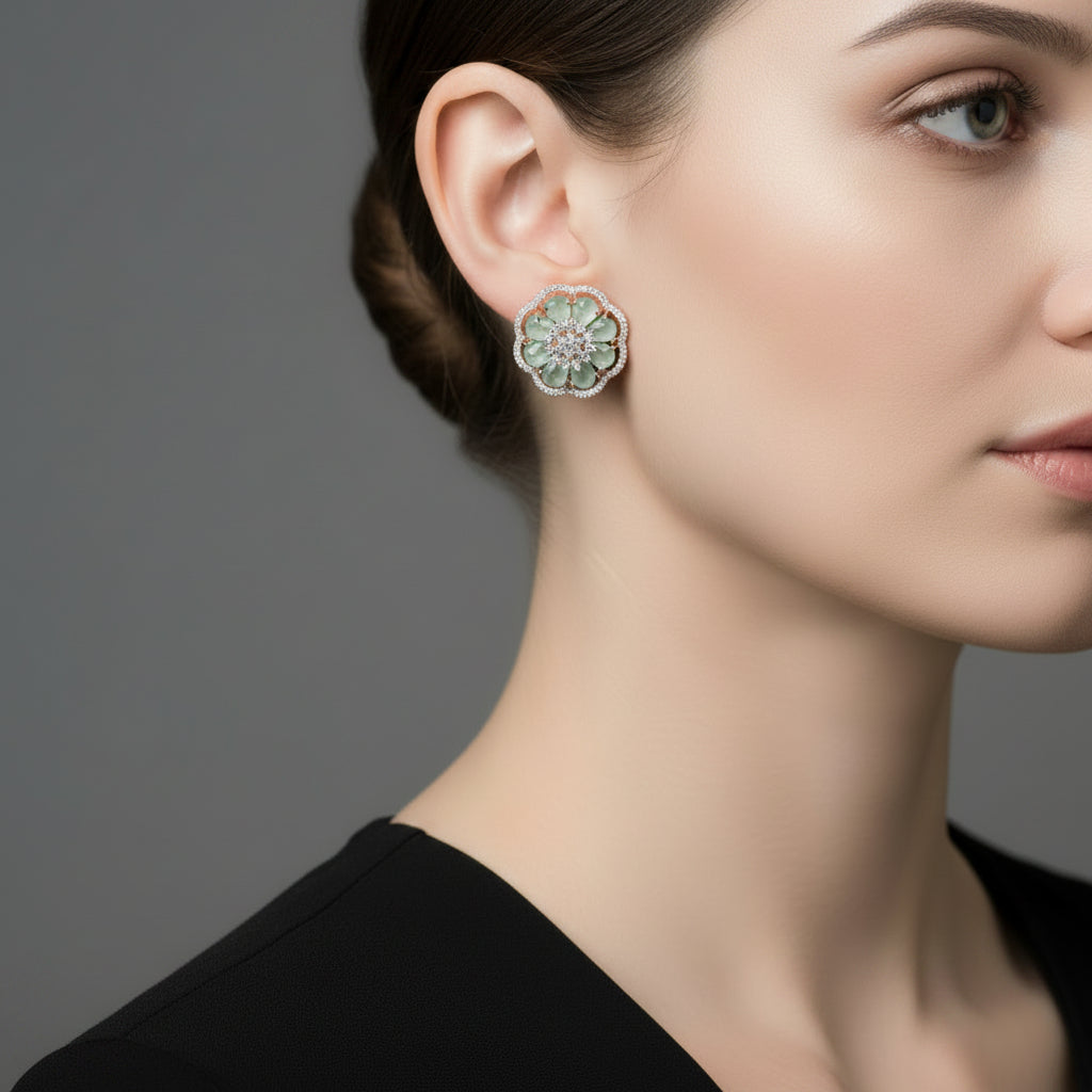 Pair of flower-shaped earrings with green gemstones on a gray surface