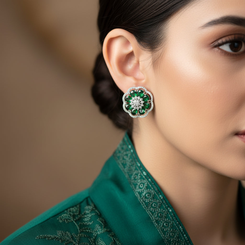 Pair of floral earrings with green and clear gemstones on a gray surface.