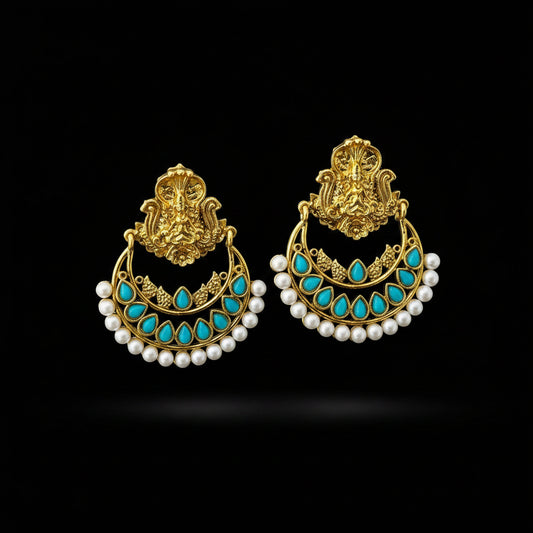 A pair of traditional Indian gold-plated earrings with turquoise blue stone accents, white faux pearl bead borders, and a detailed gold top piece, displayed on a dark reflective surface with the SAHELI brand logo above.