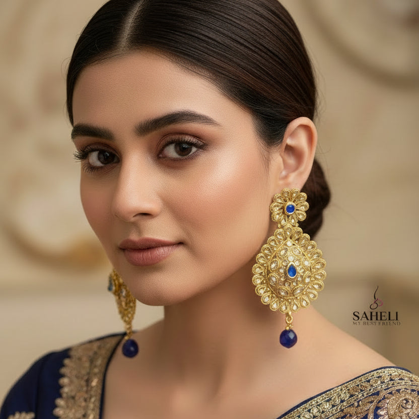Gold earrings with blue stones on a dark background, branded 'Saheli'.