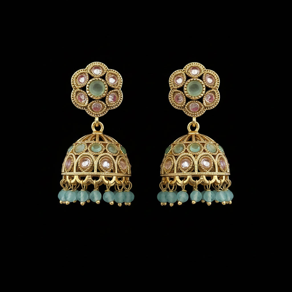 A pair of gold-plated Indian jhumka earrings decorated with light green stones, pink stones, and light blue bead drops, set against a solid dark pink background.