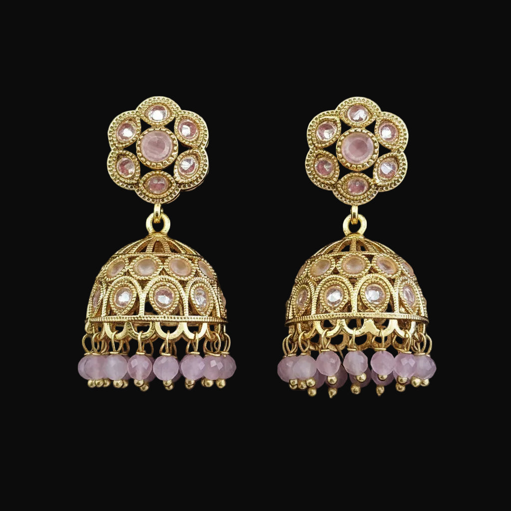 A pair of gold-plated Indian jhumka earrings with pink stone accents, displayed on a solid dark pink background.