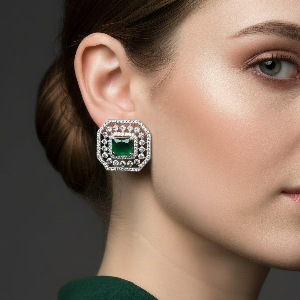 Pair of hexagonal earrings with green gemstones and diamond-studded borders on a dark background.