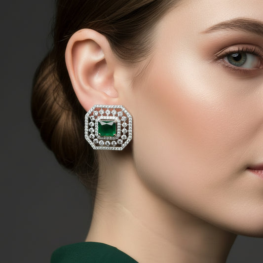 Pair of hexagonal earrings with green gemstones and diamond-studded borders on a dark background.