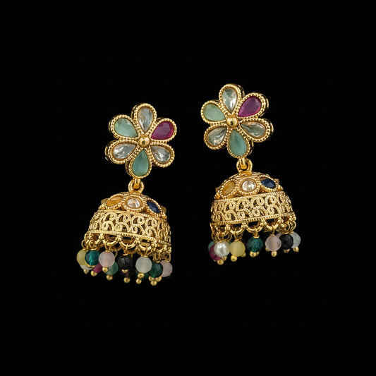 A pair of gold-plated Indian jhumka earrings with floral stud tops and dangling bell-shaped charms, shown on a solid teal-green background.