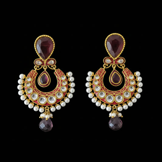 A pair of traditional Indian gold-plated chandelier earrings with deep red enamel, white pearl bead borders, and teardrop-shaped dark red gemstones, displayed on a dark reflective surface with the brand logo 'SAHELI MY BEST FRIEND' above them.