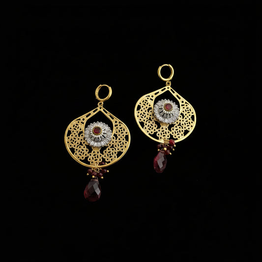 Gold earrings with red gemstones on a dark background, featuring the brand 'Saheli'.