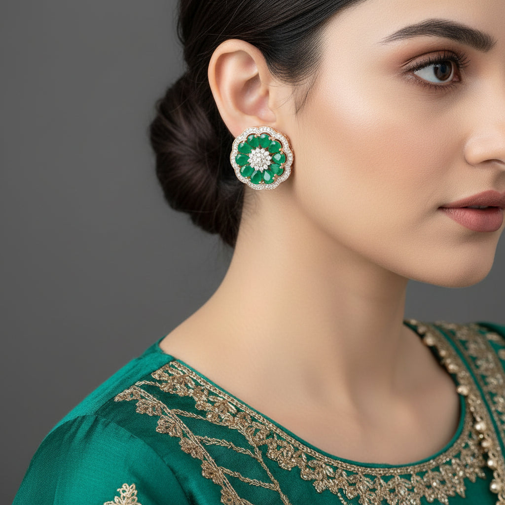 Pair of floral earrings with green gemstones and clear centers on a dark background, branded 'SAHELI'.