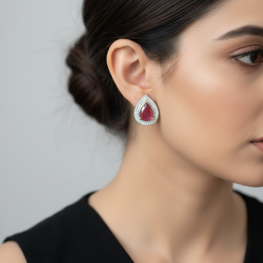 Teardrop-shaped earrings with red gemstones and silver frames on a dark background, branded 'Saheli'.