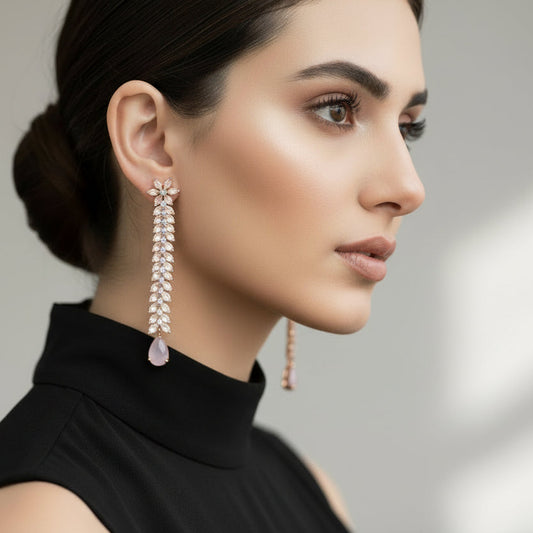 Pair of long, leaf-like earrings with pink teardrop stones on a dark background