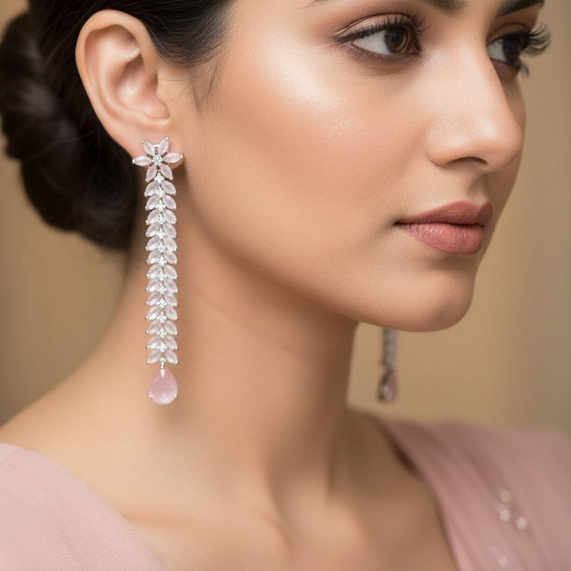 Pair of long earrings with floral designs and pink teardrop stones on a dark background