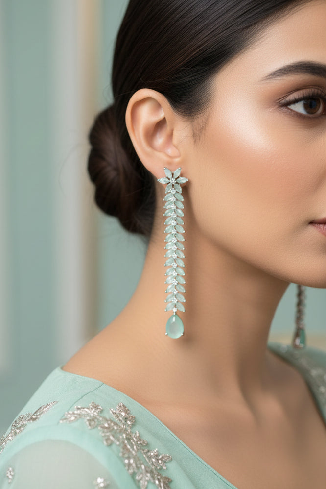 Pair of long, decorative earrings with floral designs and teardrop-shaped elements on a dark background.
