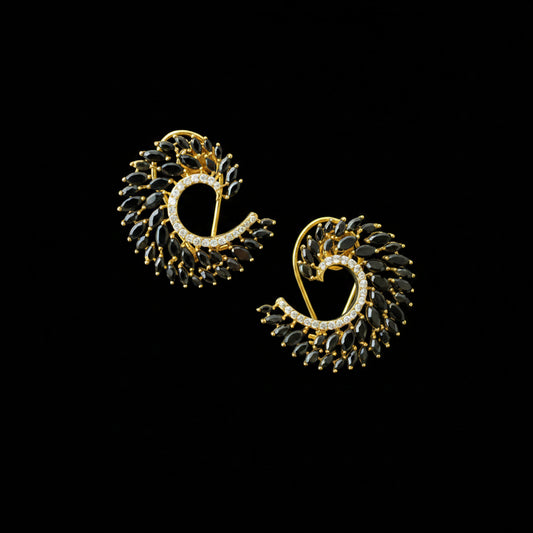 A pair of gold-plated crescent-shaped earrings decorated with black marquise-cut crystals and a row of small clear stones, displayed on a dark reflective surface with the SAHELI MY BEST FRIEND logo in the top left corner.