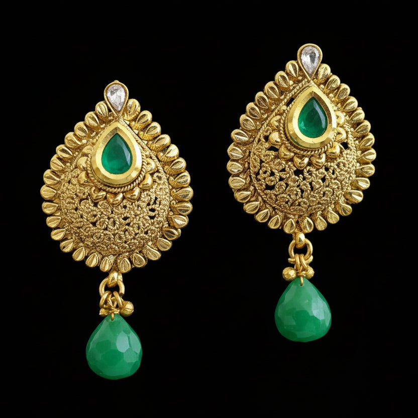 Gold earrings with green drops on a gray stand, branded 'Saheli'.