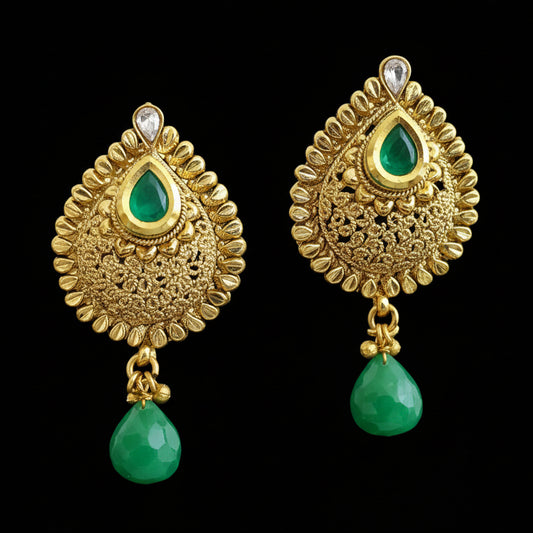 Gold earrings with green drops on a gray stand, branded 'Saheli'.