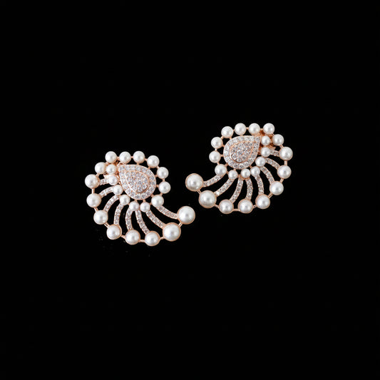 A pair of ornate pearl and rose gold earrings with a floral or fan-like design, displayed on a dark reflective surface.