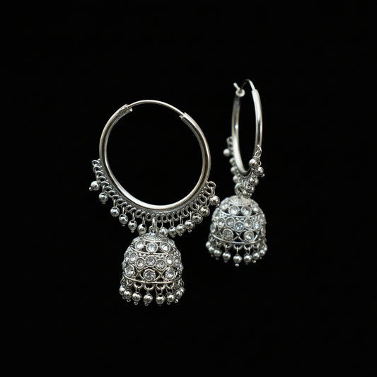 Silver hoop earrings with jhumka designs on a black stand against a dark background
