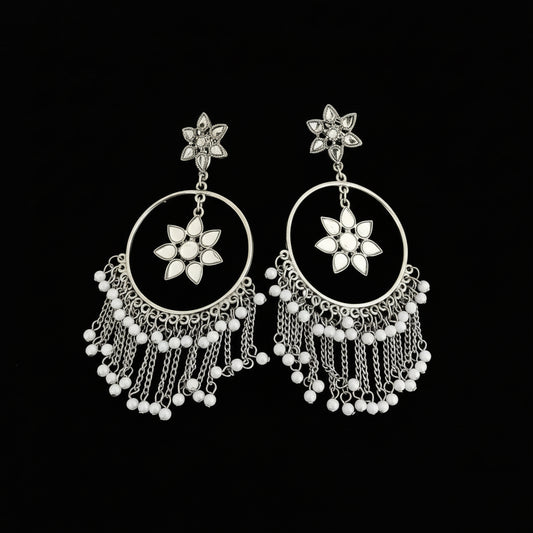 Pair of silver earrings with floral designs and dangling beads on a reflective surface.
