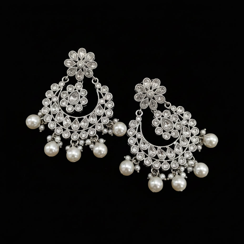 A pair of silver-toned filigree chandelier earrings with white faux pearls, displayed next to a small clear plastic bag containing a matching pair of gold-toned filigree earrings with pearls.