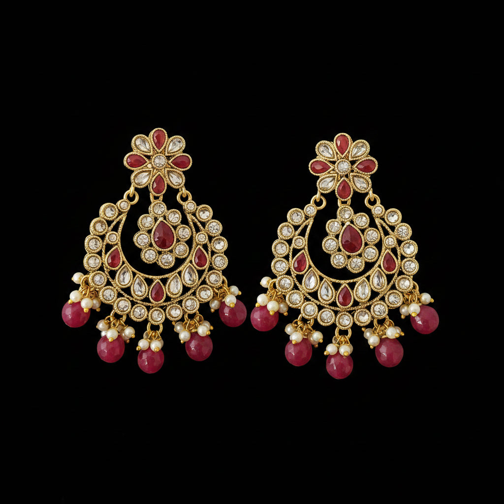 Ornate gold earrings with red gemstones on a dark background, featuring the brand 'Saheli'.