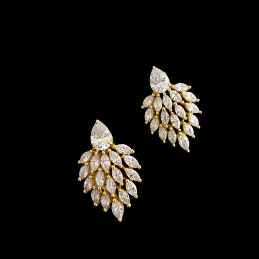 Gold and diamond earrings on a gray background with 'Saheli' brand logo.