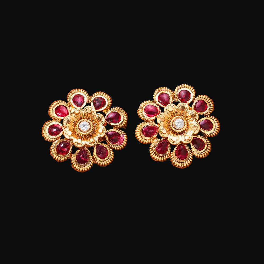 Pair of gold and red gemstone earrings on a brown textured background