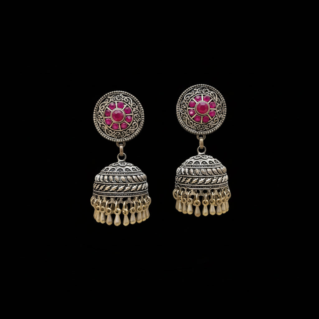 Ornate silver earrings with pink stones on a gray stand, branded 'Saheli'.