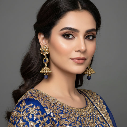 Gold and blue gemstone earrings on a gray stand with 'SAHELI' branding.
