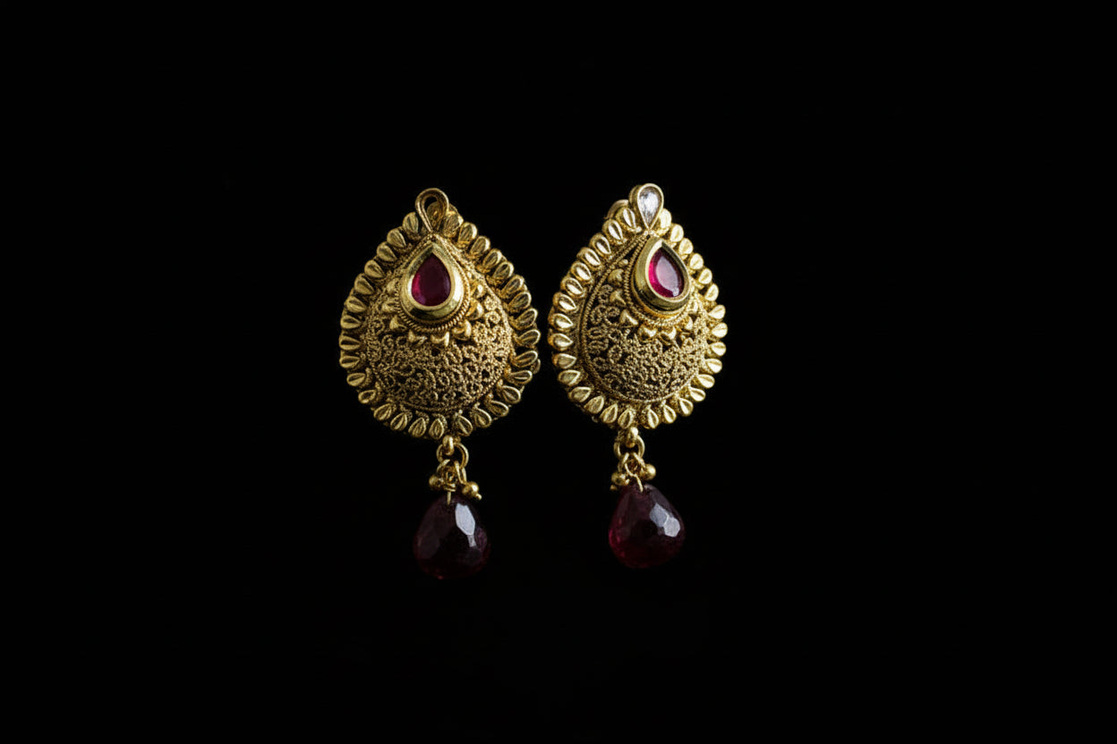 Gold earrings with red gemstones on a dark background, featuring the brand 'Saheli'.