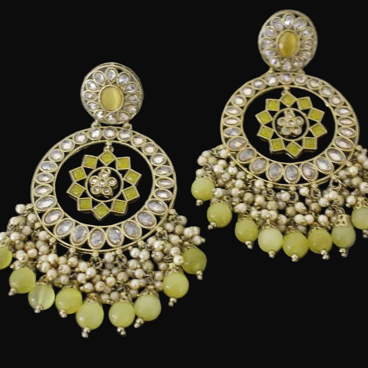 Ornate earrings with green stones on a dark background, branded 'SAHELI'.