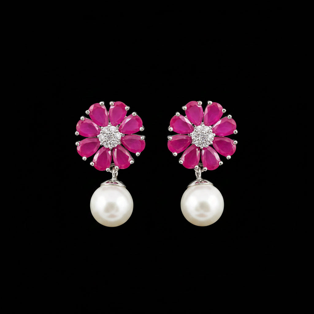 A pair of flower-shaped drop earrings with bright pink gemstone petals, silver-toned metal settings with clear stones in the center, and hanging white pearl drops, displayed on a black stand against a gray background. The brand name 'SAHELI MY BEST FRIEND' is visible at the top.