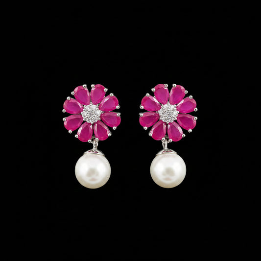 A pair of flower-shaped drop earrings with bright pink gemstone petals, silver-toned metal settings with clear stones in the center, and hanging white pearl drops, displayed on a black stand against a gray background. The brand name 'SAHELI MY BEST FRIEND' is visible at the top.