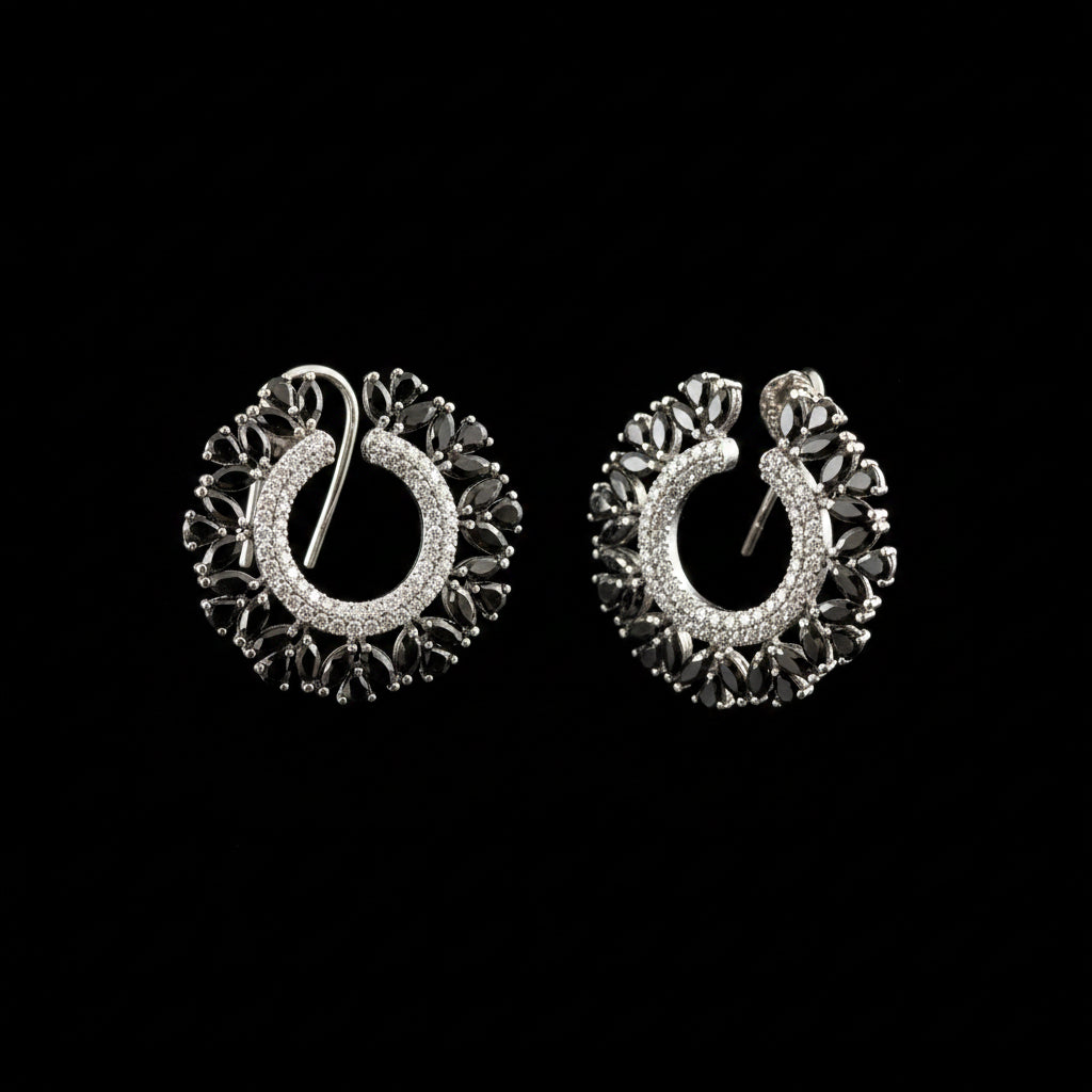 A pair of silver crescent-shaped hoop earrings with intricate filigree detailing and clear stones, displayed on a dark reflective surface with the brand logo 'SAHELL MY BEST FRIEND' above them.