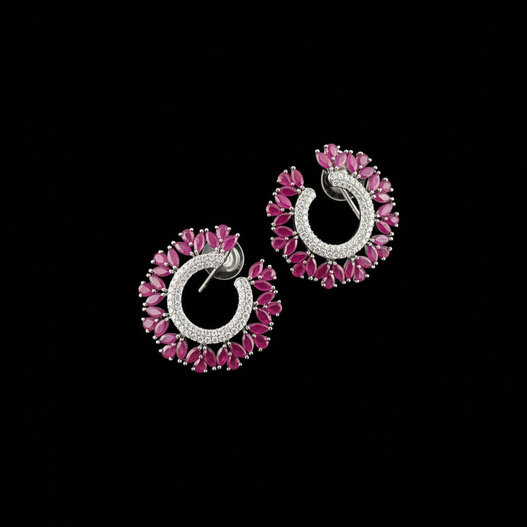 A pair of silver crescent-shaped earrings adorned with bright pink marquise-cut stones and a halo of clear cubic zirconia, displayed on a dark reflective surface with the SAHELI MY BEST FRIEND logo above.