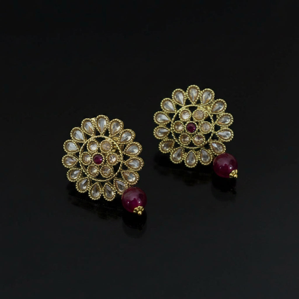 Pair of gold floral earrings with red gemstones on a dark background