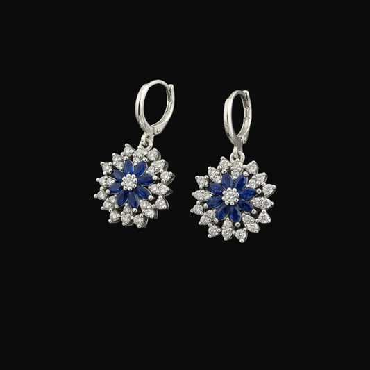 Pair of silver earrings with blue and white stones on a gray background, branded 'Saheli'.