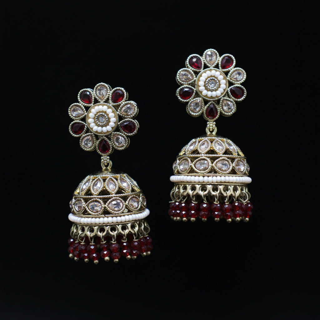 Pair of ornate earrings with floral designs and red gemstones on a black background