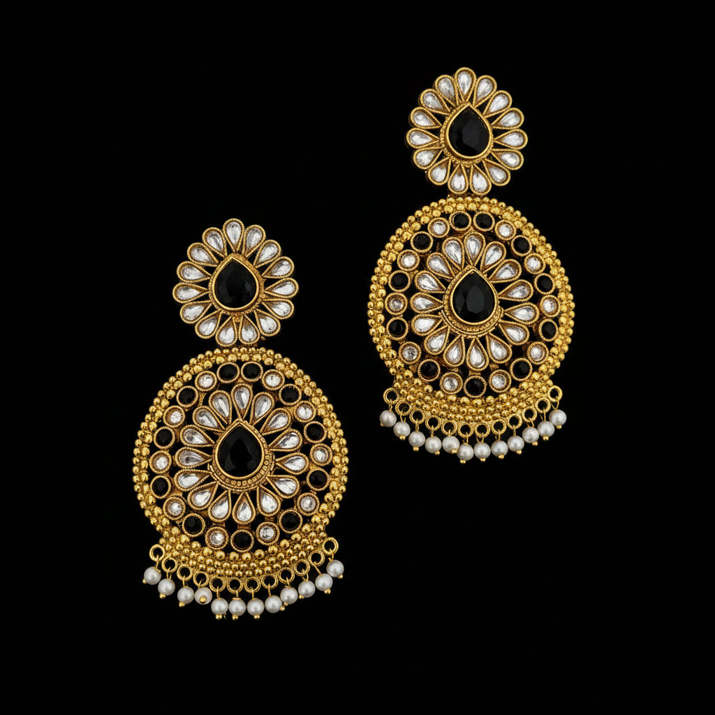 A pair of ornate gold-toned Indian jhumka earrings decorated with black teardrop stones and white faux pearl accents, displayed on a dark gray reflective surface with the brand logo 'SAHELI MYBESTFRIEND' at the top.